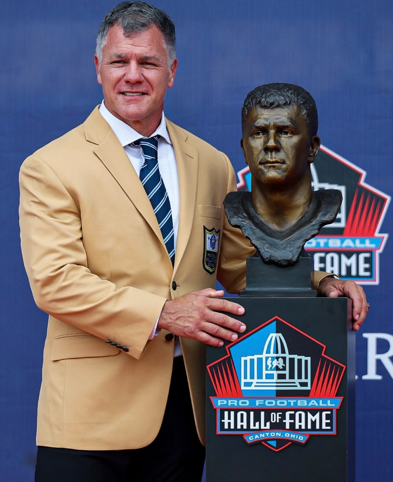 Adam Vinatieri standing with his portrait bust at the Pro Football Hall of Fame